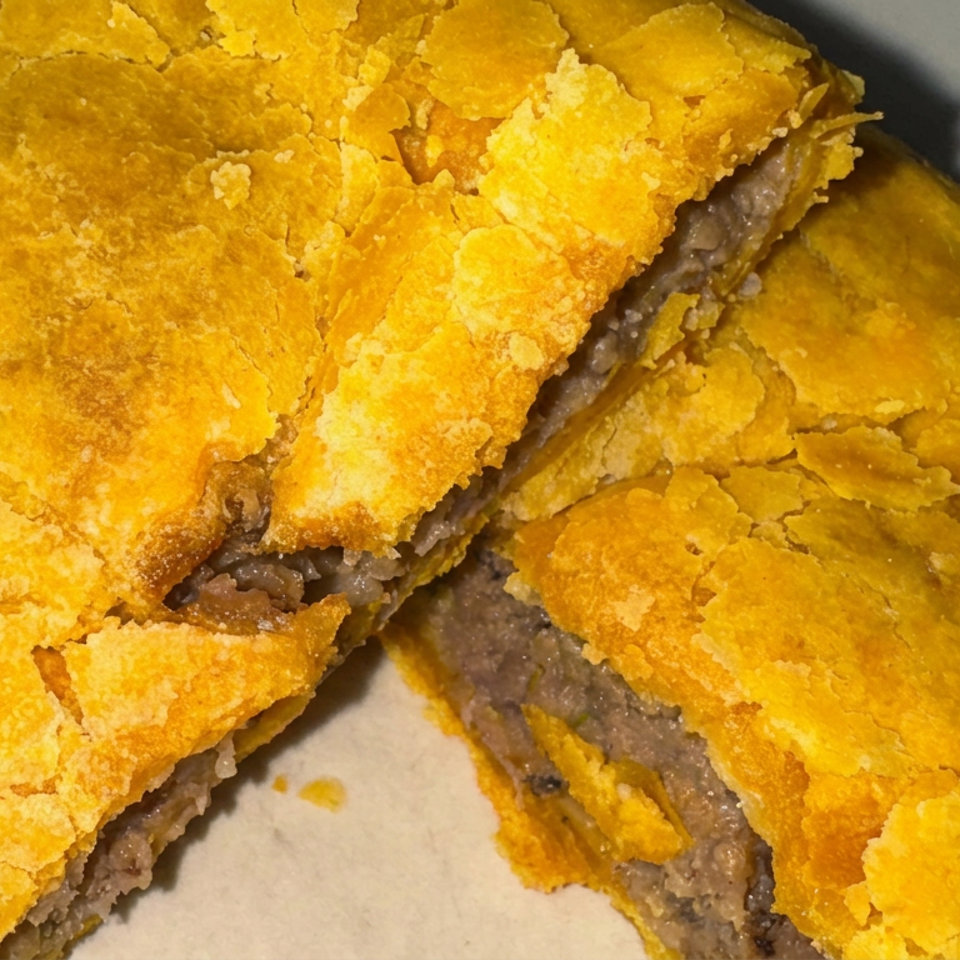 Close-up of a golden flaky pastry filled with seasoned ground meat, sliced open on a plate.